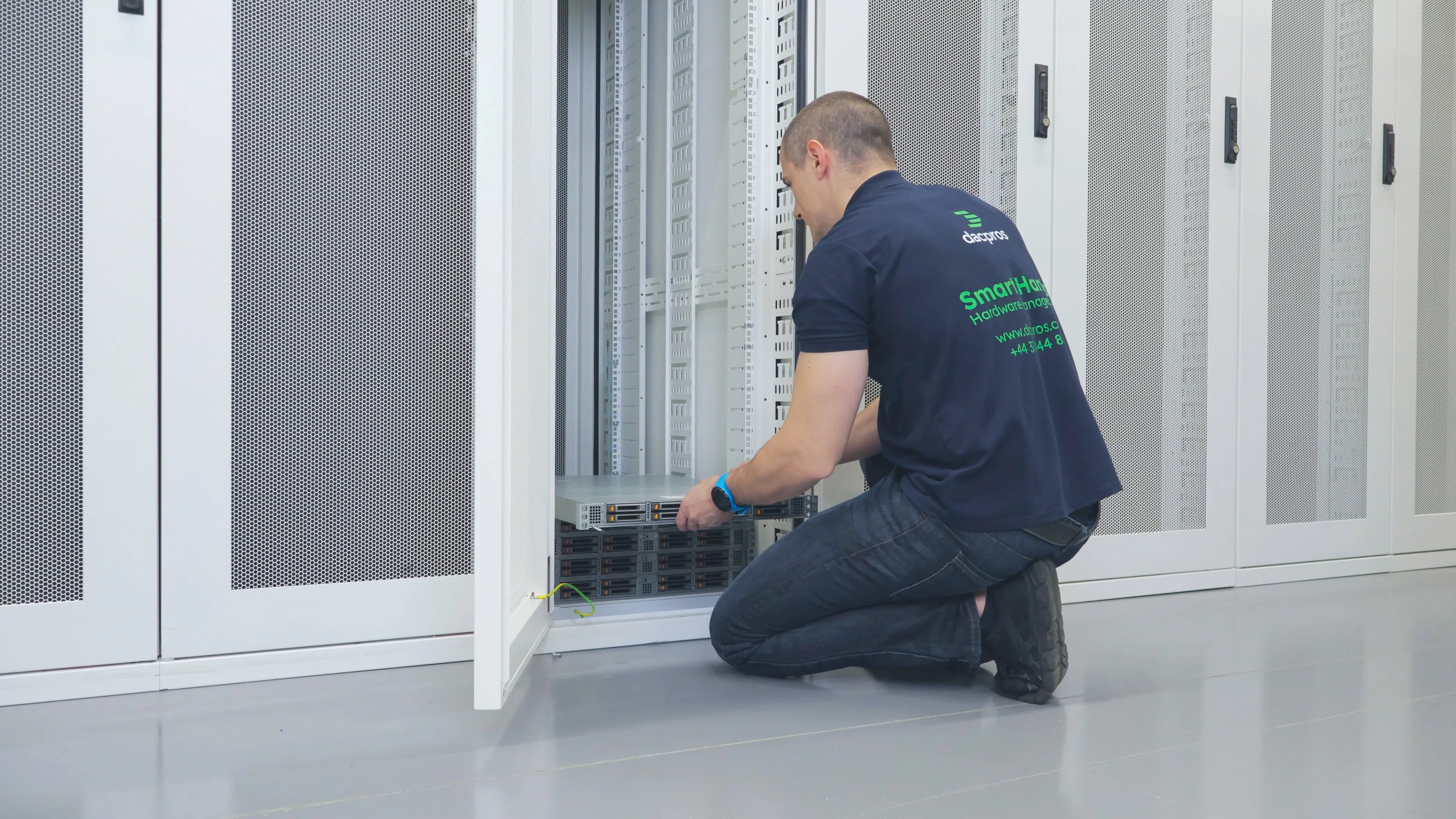 DACPROS engineer kneeling at an open rack, working on equipment at the base of a server cabinet